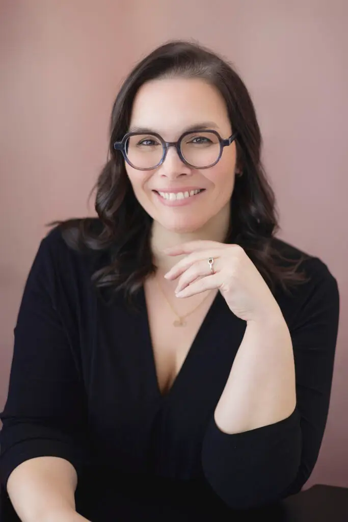 Portrait de Véronique Julien, conférencière et auteure, souriante, la main sous le menton, sur fond vieux rose